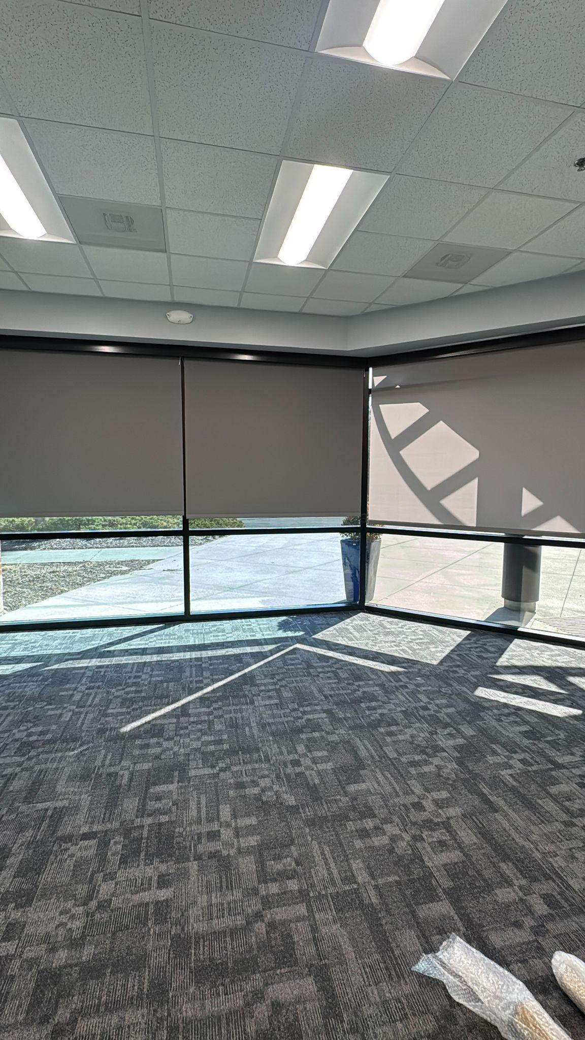 Interior roller shades partially drawn in a room with large windows and patterned carpet.